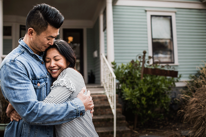 An Asian couple hugs outside their newly purchased home.