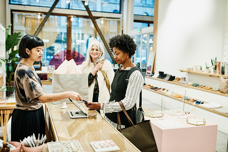 a woman makes a purchase with help from a salesperson while another woman smiles