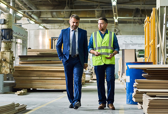A male business owner walks alongside a warehouse worker in surrounded by lumber.