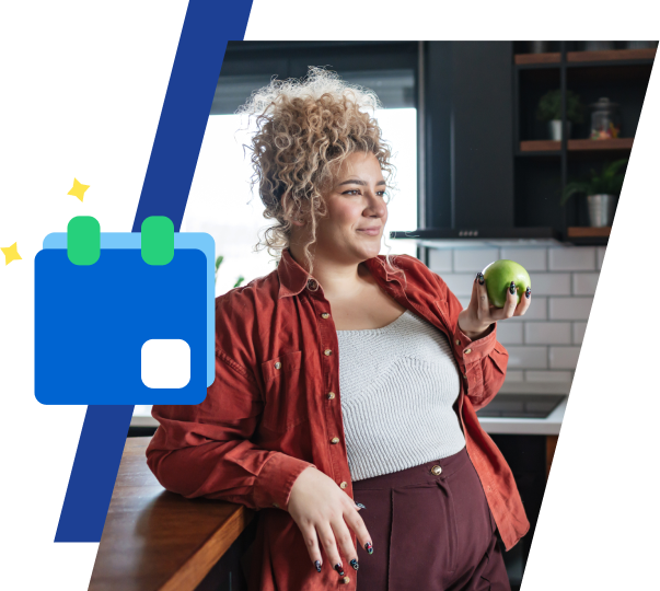 a curly haired woman holds an apple and leans on a countertop